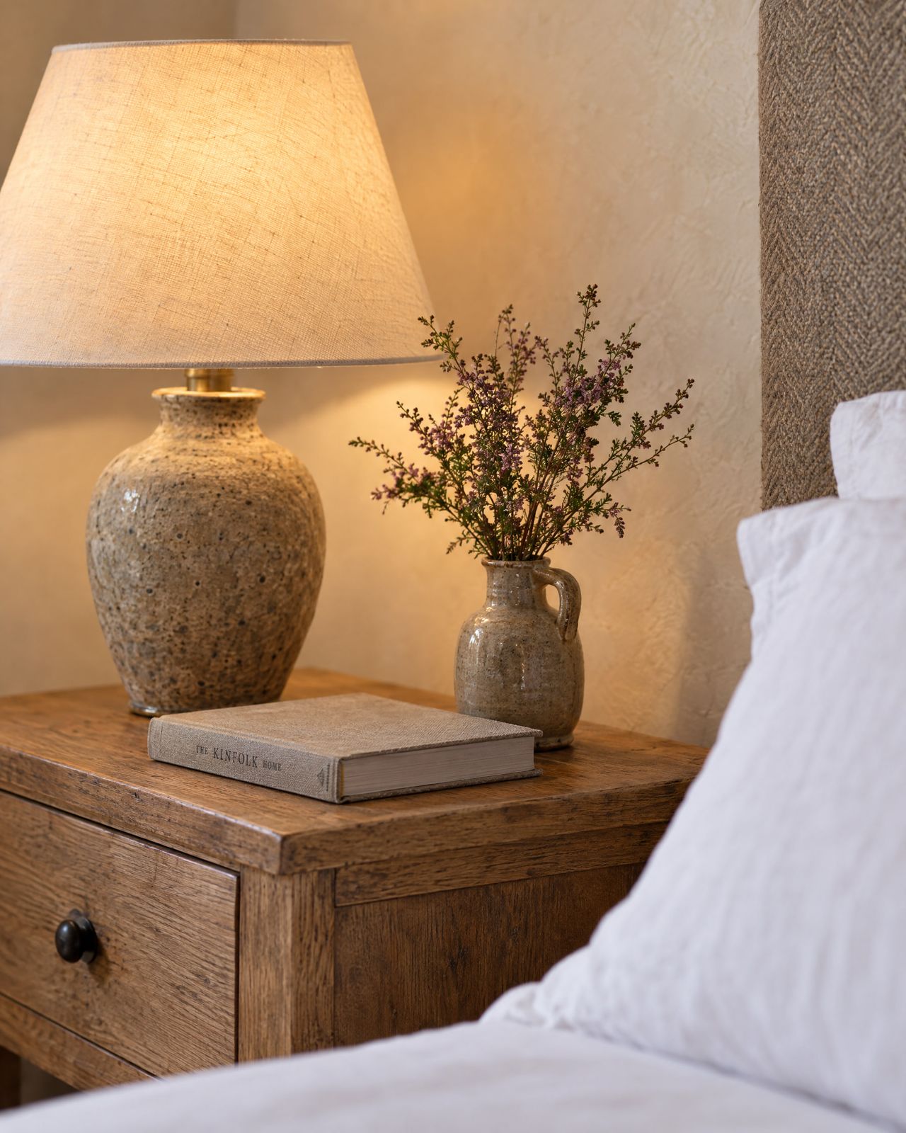 A stoneware lamp, a book and wild heather on the oak bedside table.