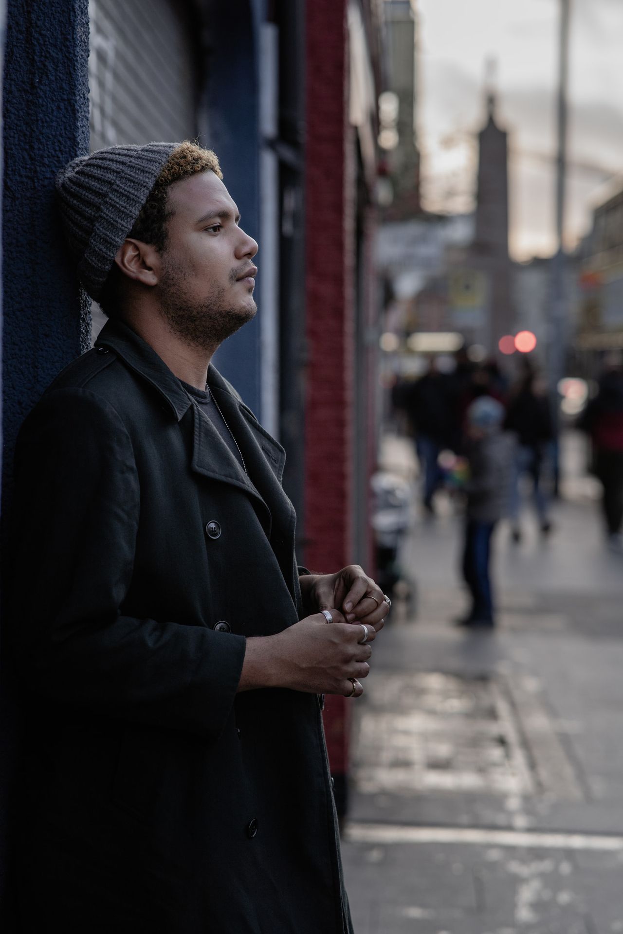 In profile against a blue shop front, wearing a grey beanie, the street busy behind.