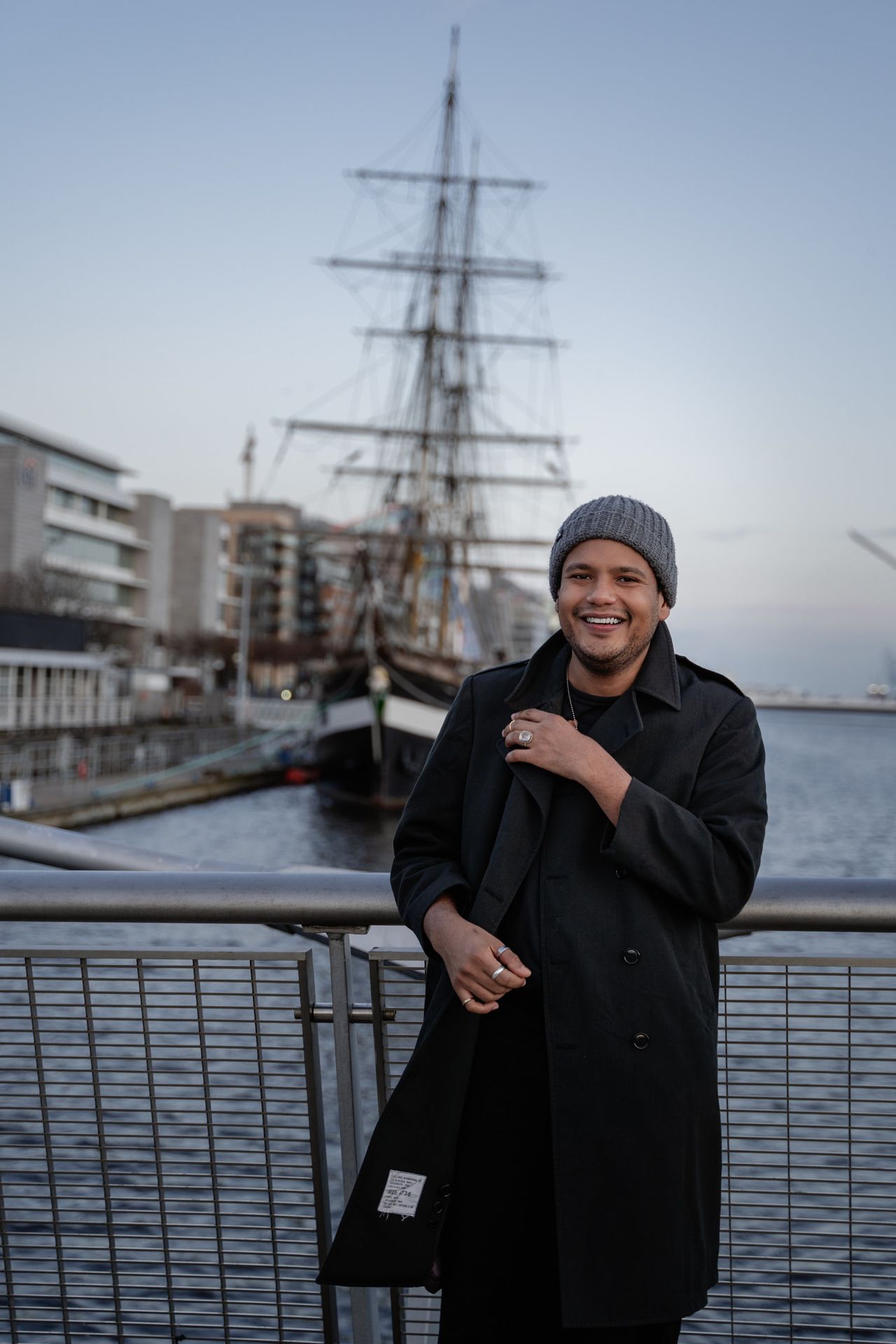 Laughing by the river railings, a tall ship moored behind.