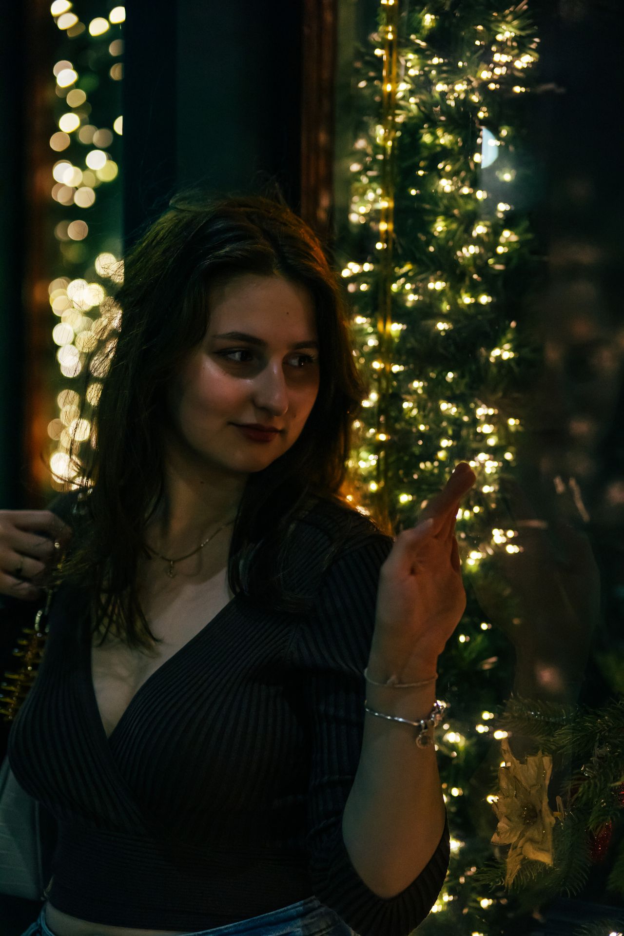 Between two columns of fairy lights, the face lit warm, one hand raised.