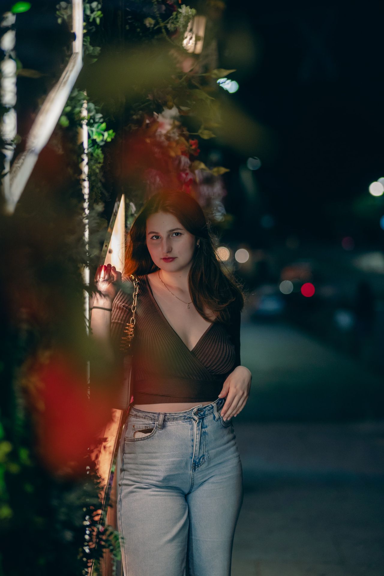 At night behind blurred red flowers, the street lights soft beyond.
