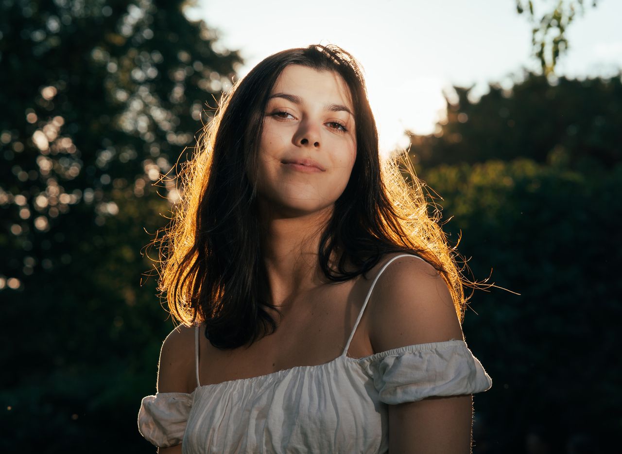 Backlit by the low sun among summer trees, the hair edged with light, a slight smile at the camera.