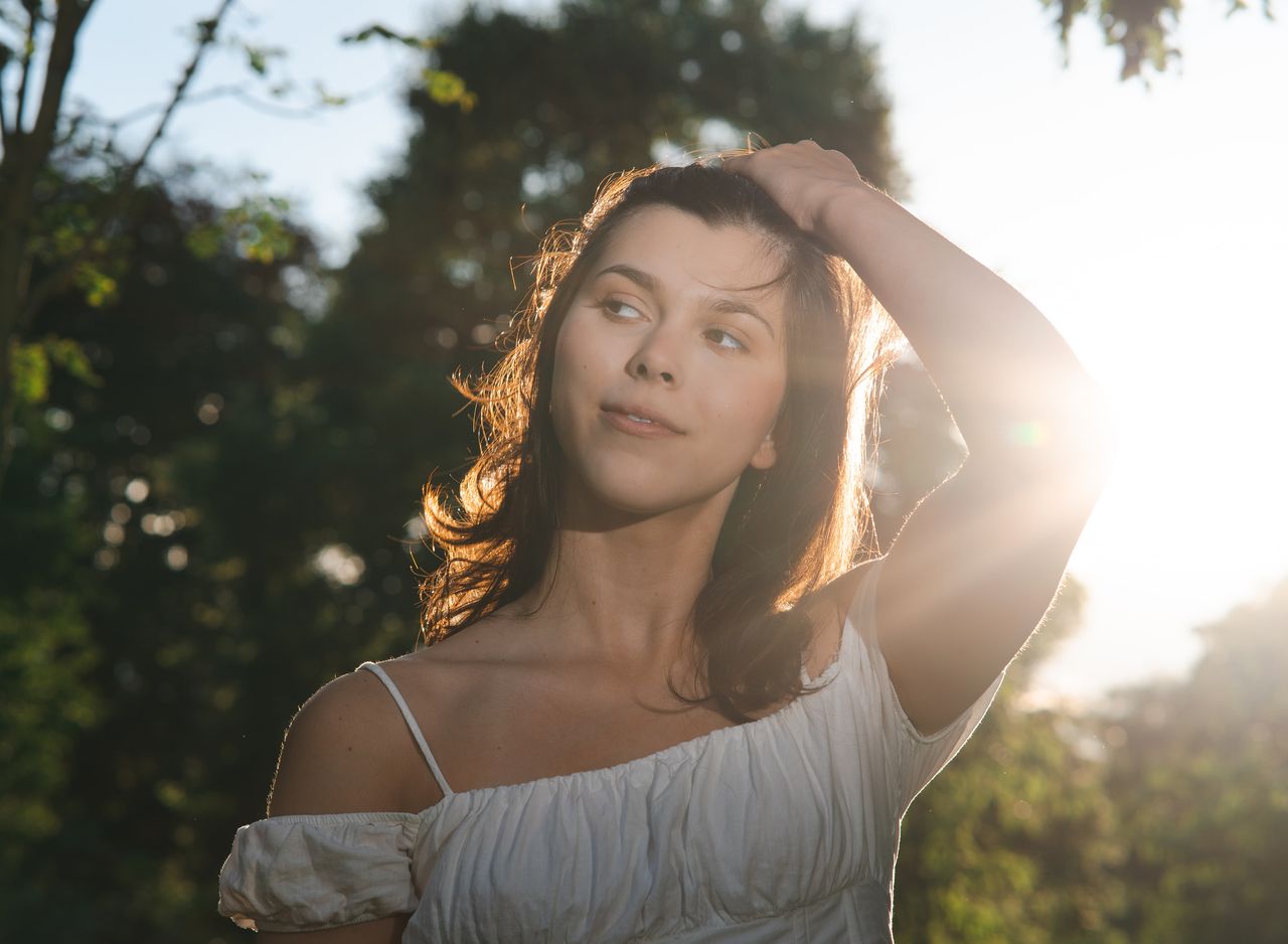 One hand in the hair, the sun flaring behind the raised arm.