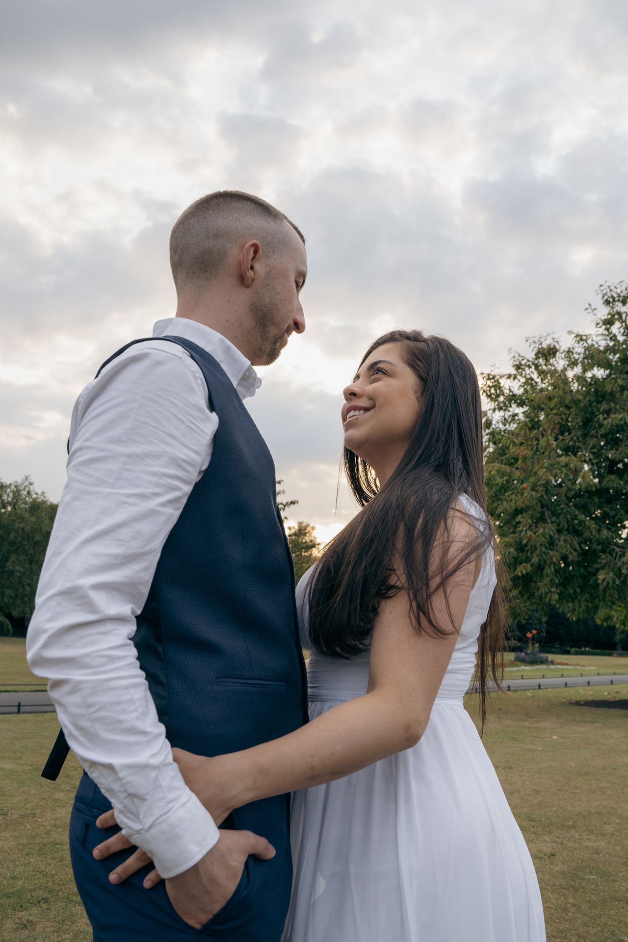 Close together under the clouds, one hand on a hip, sharing a smile.