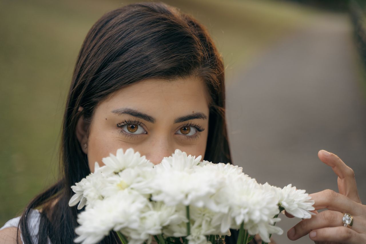 Eyes above a bunch of white flowers, a ring on the hand that holds them.