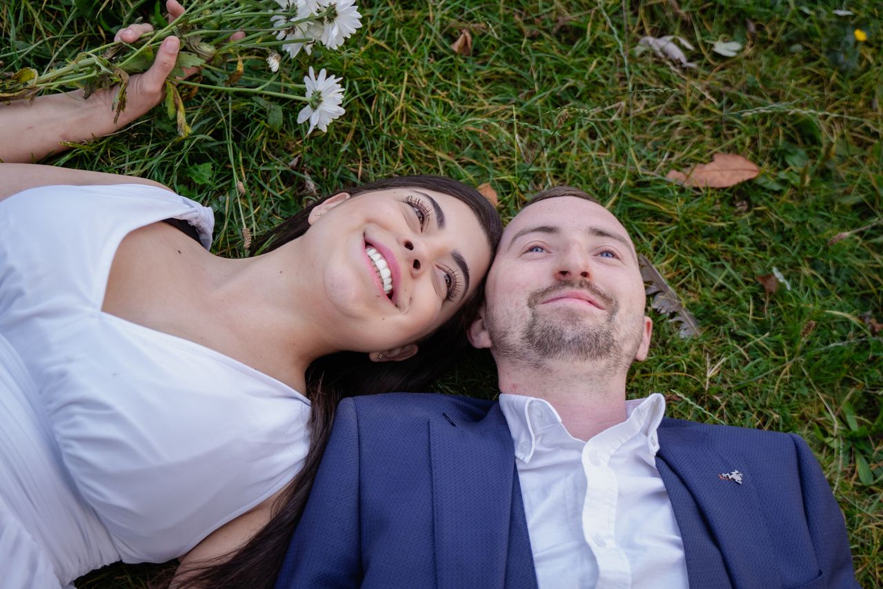 Lying head to head in the grass with a handful of daisies, both smiling.