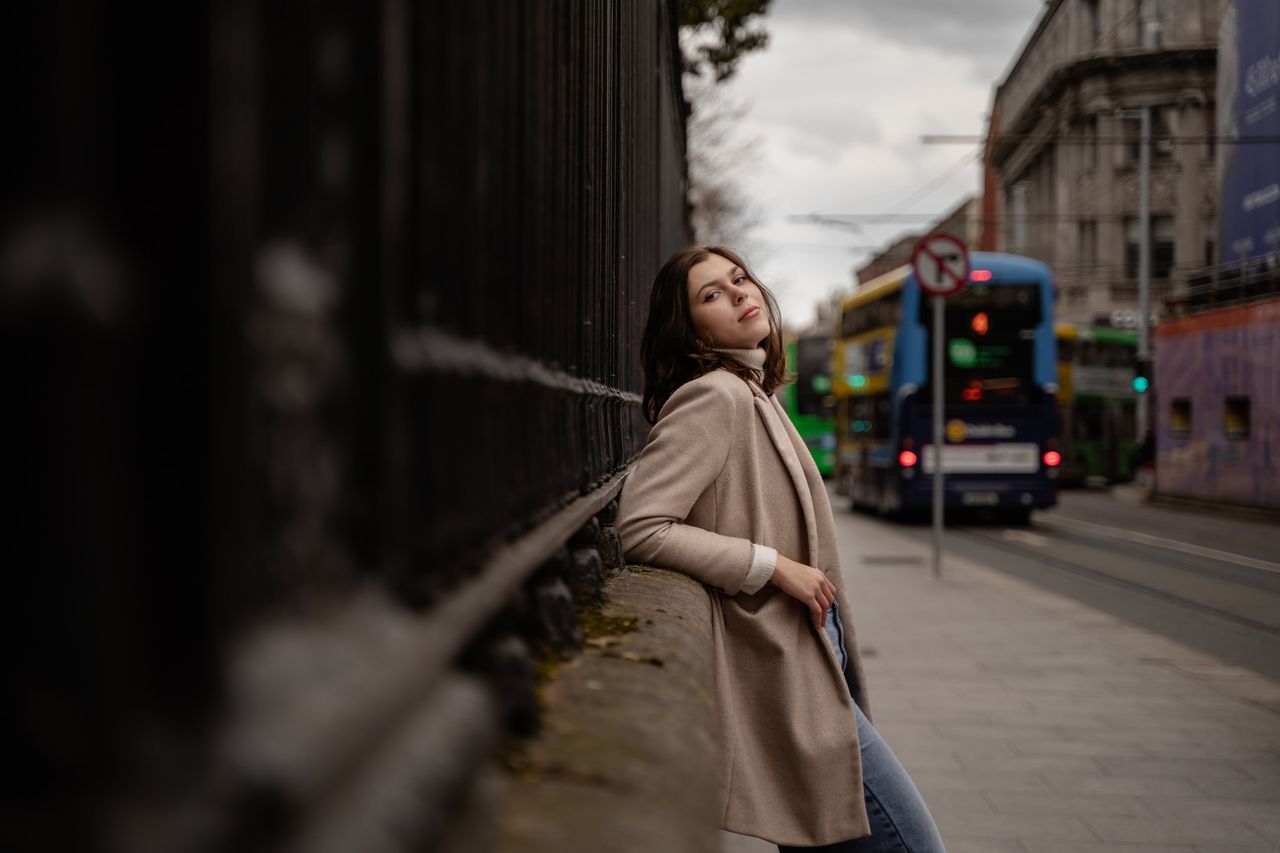 Leaning on a stone wall under black railings while a double-decker bus goes by.
