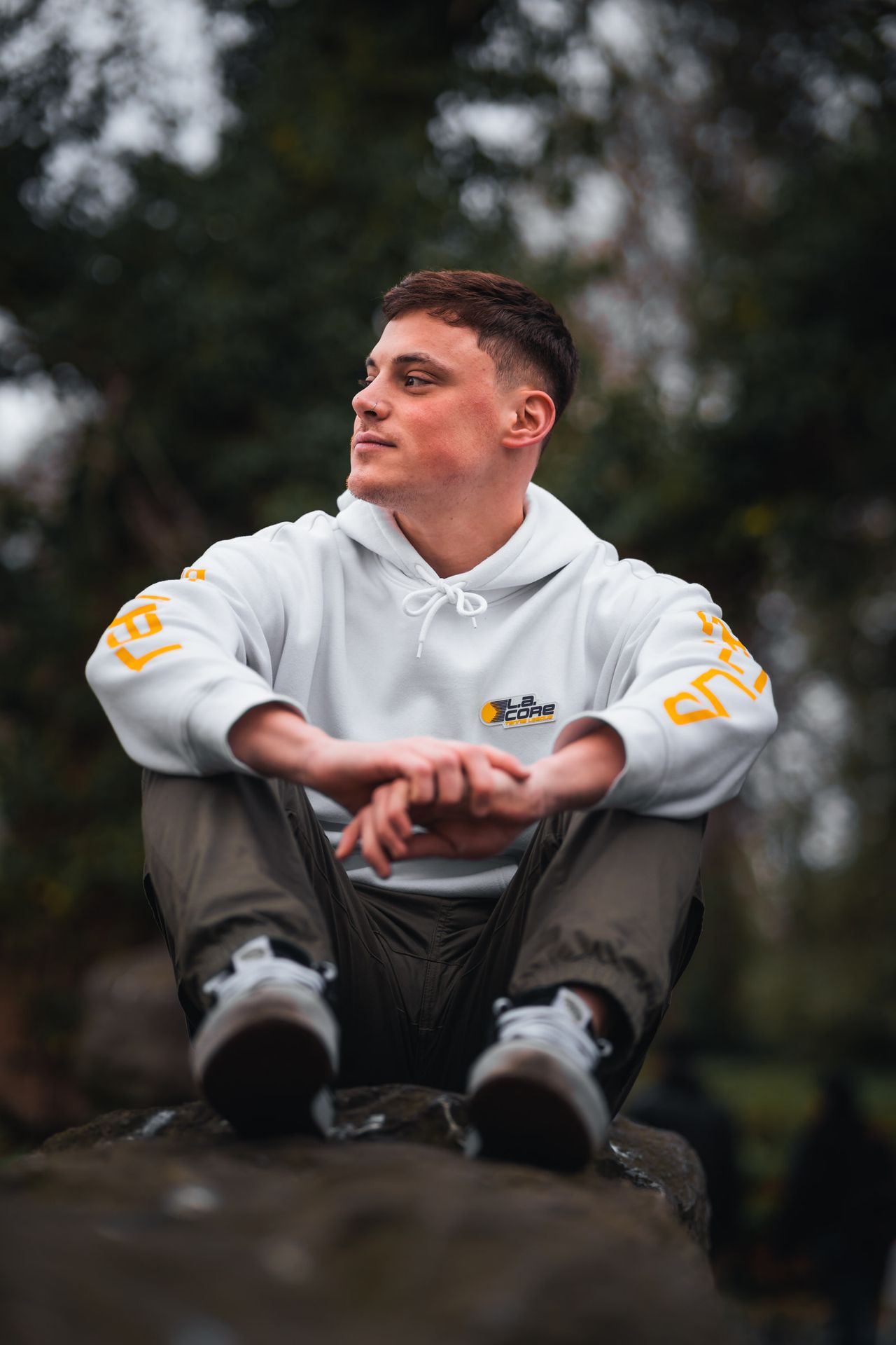 Sitting on a stone wall in a white hoodie, looking away to one side.