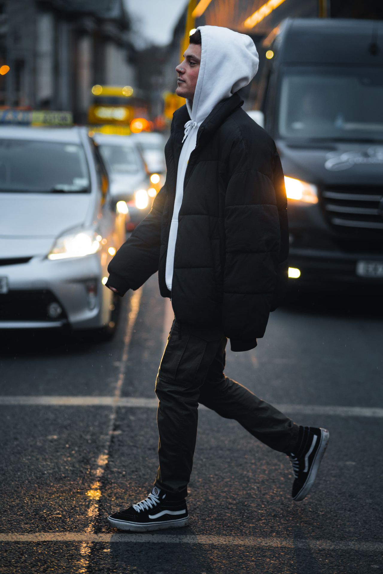 Crossing between cars and headlights in a puffer jacket, hood up.