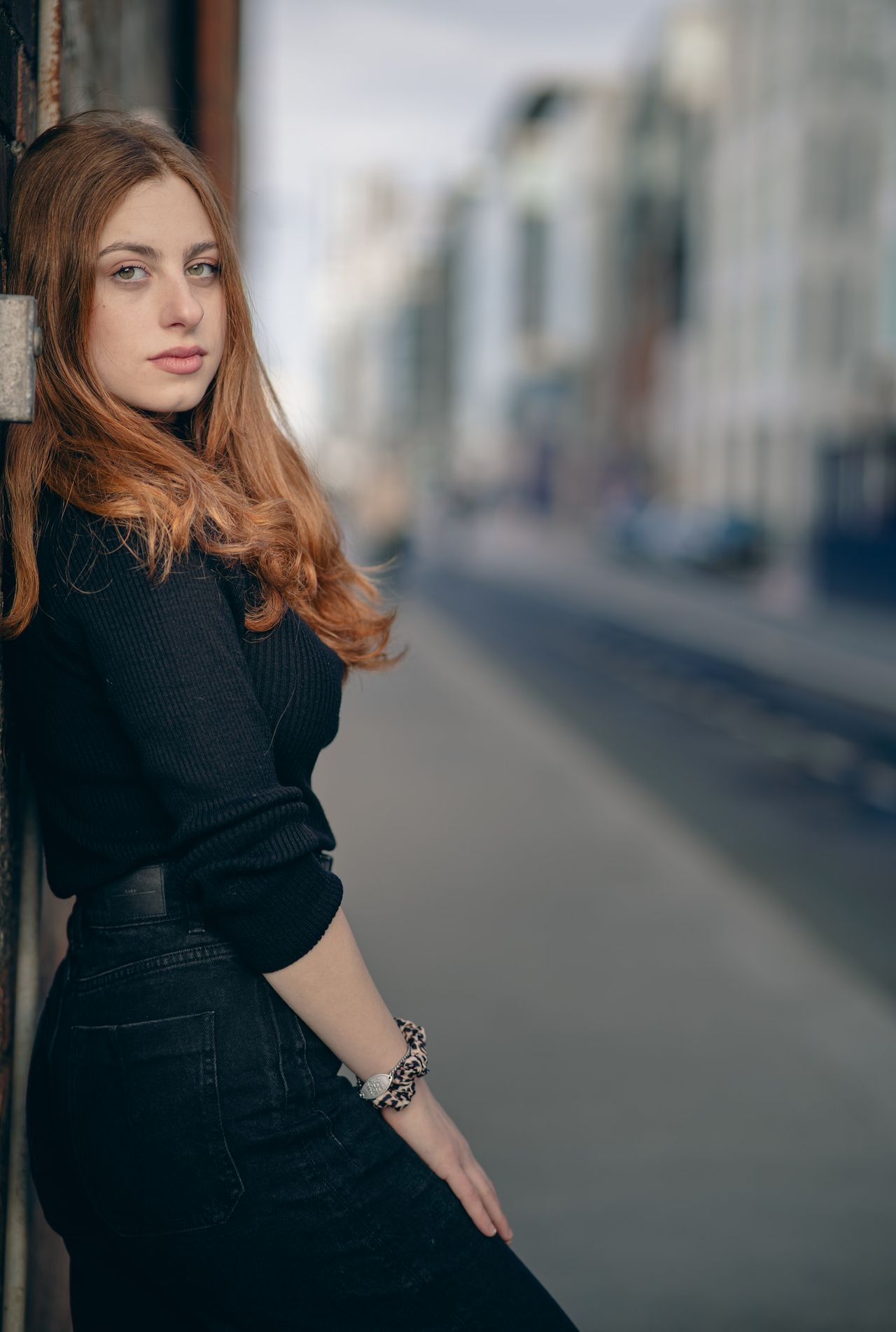 Leaning against a doorway on a long city street, looking back at the camera.