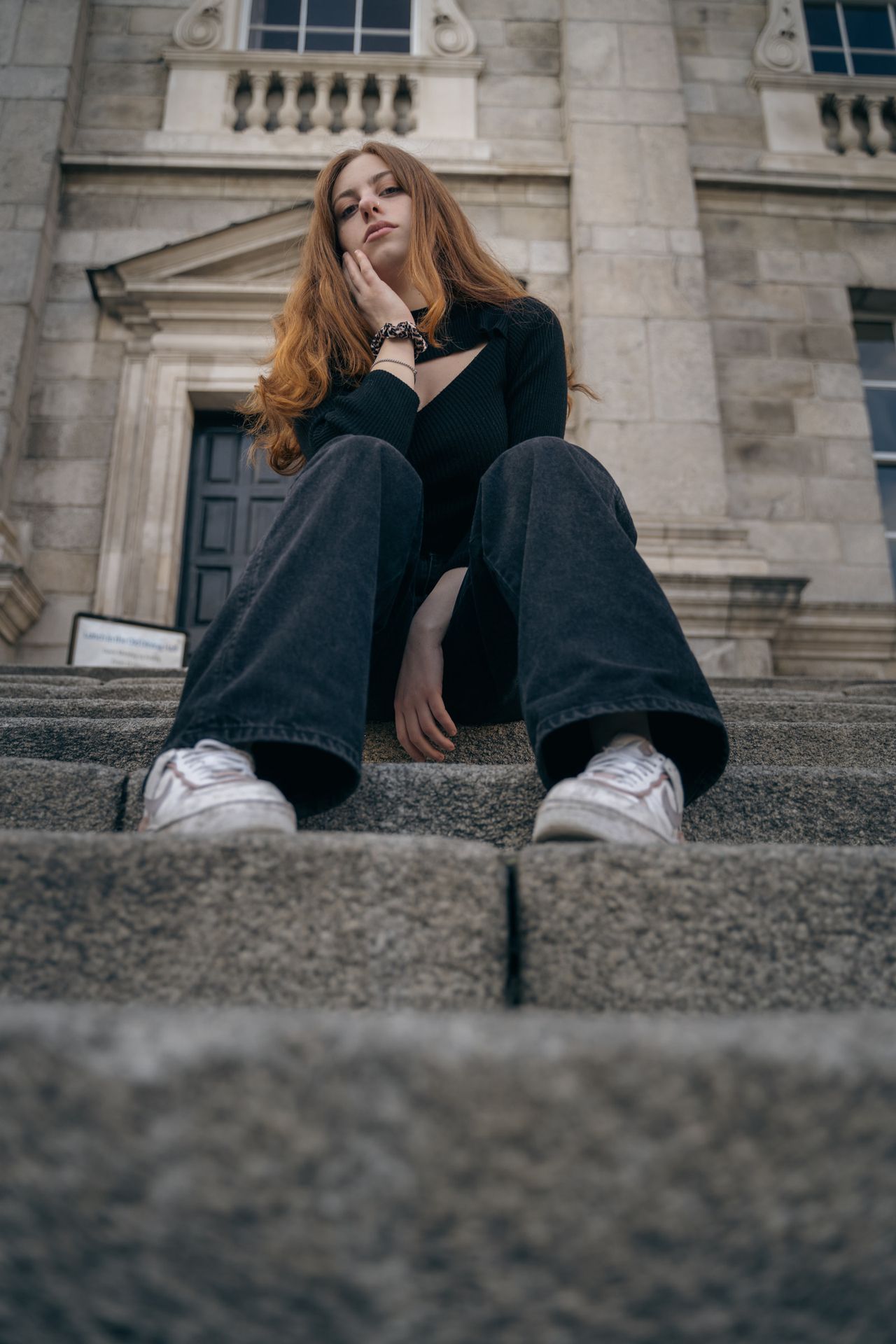 Sitting on wide stone steps in front of a classical doorway, chin resting on one hand.