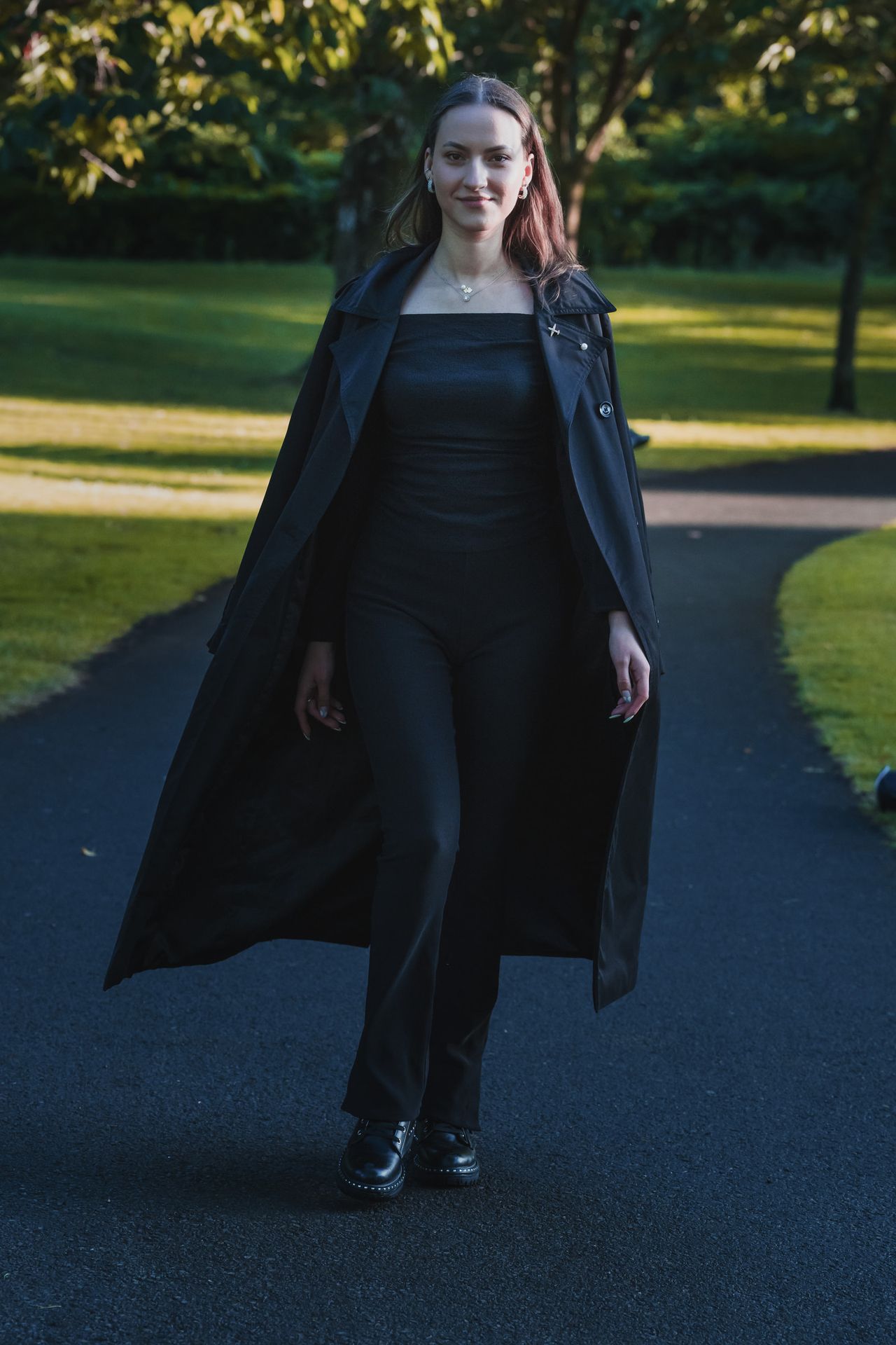 Walking towards the camera along a park path, coat open.