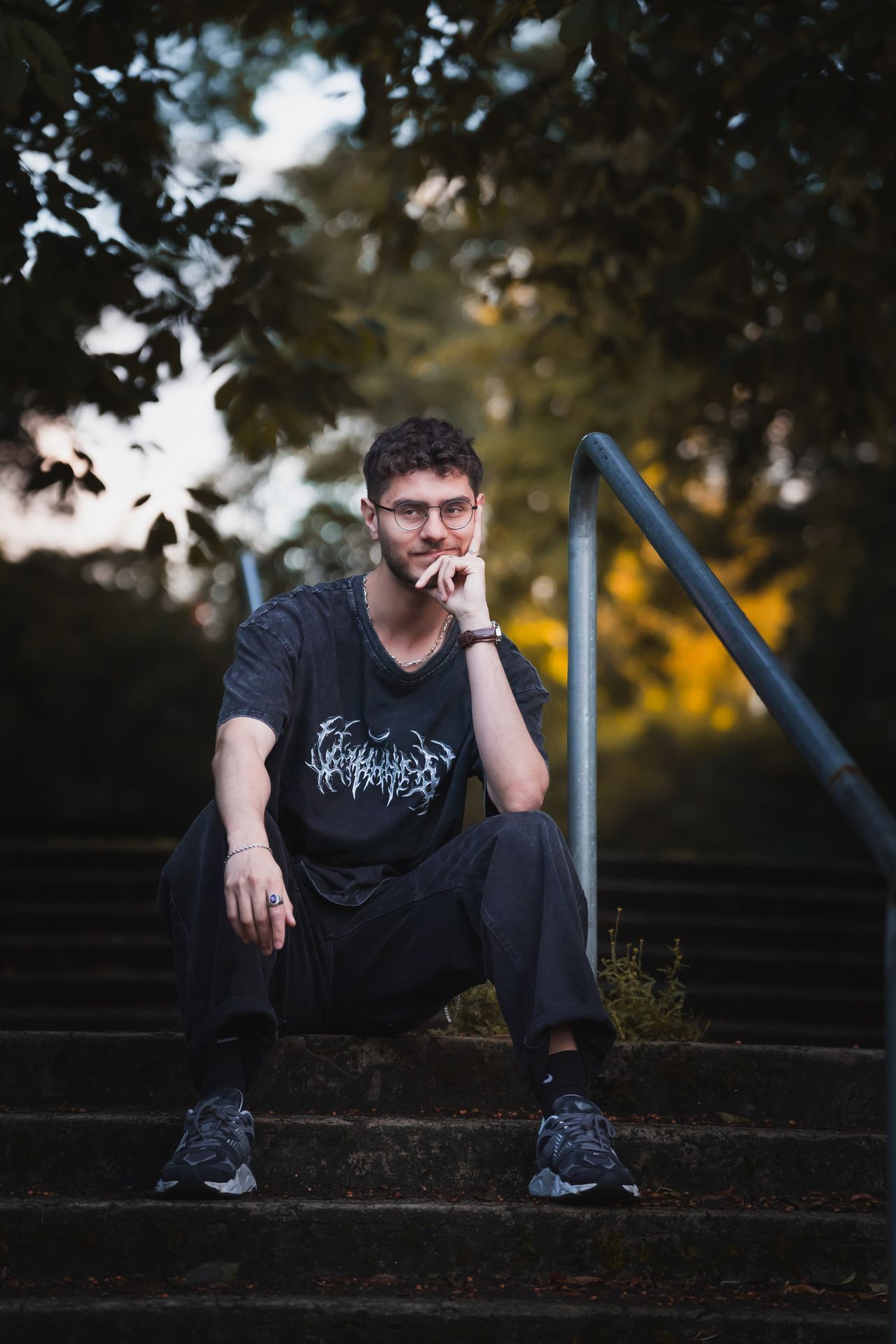 Sitting on outdoor steps beside a metal handrail, chin on one hand.
