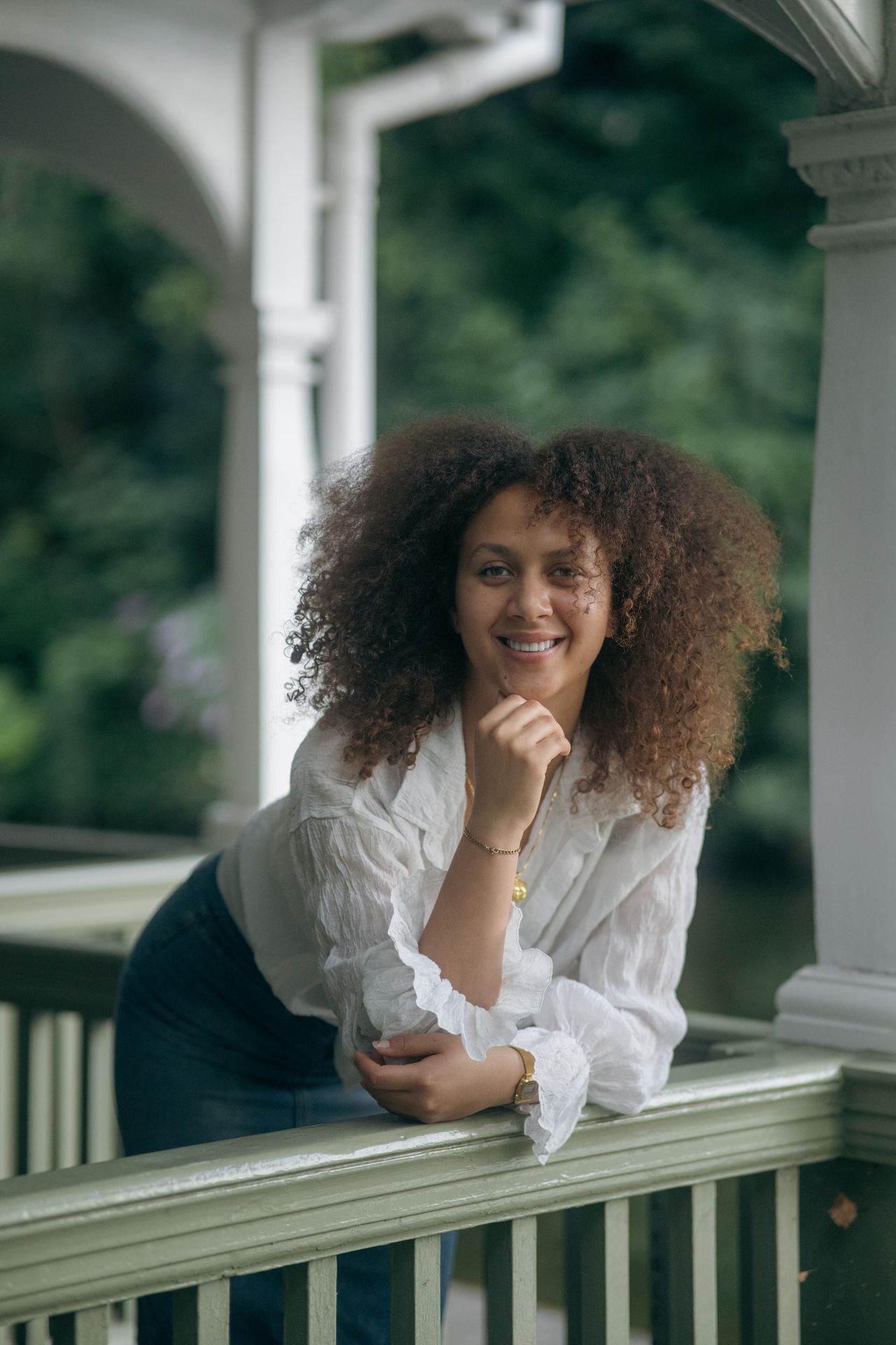 Leaning on the railing of a white wooden pavilion, chin on one hand, smiling.