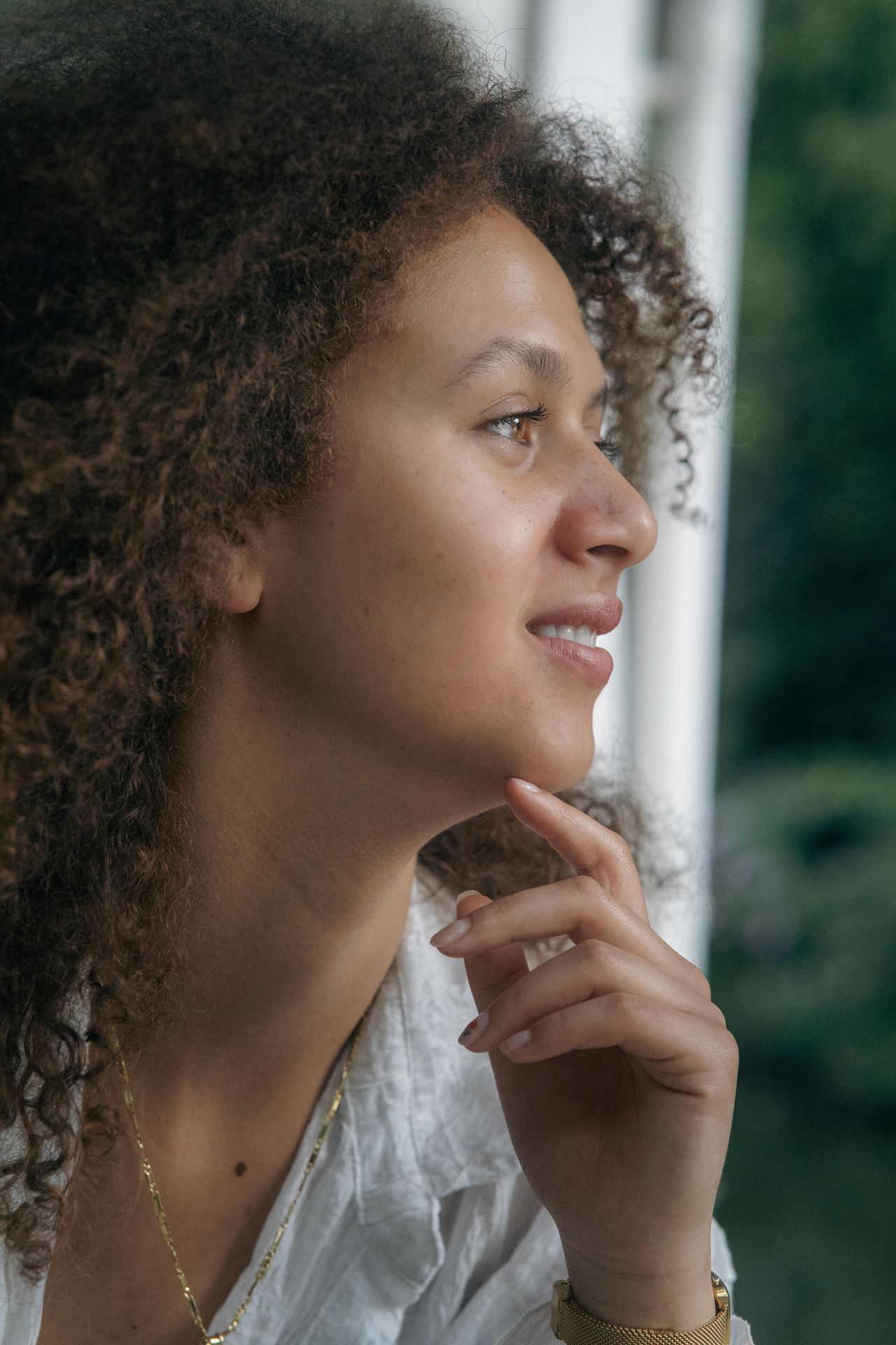 Profile in soft light, fingertips under the chin, looking out of the frame.